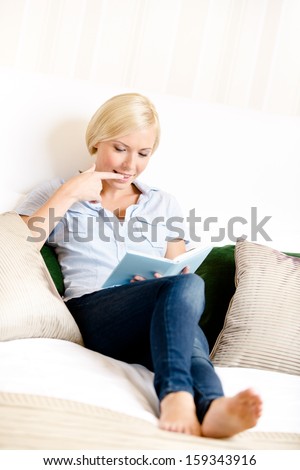 Woman sitting on the sofa reads a book. Concept of education and useful pastime