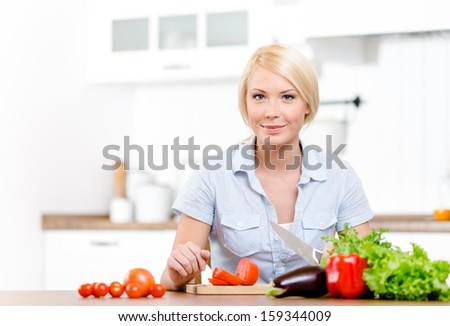 Woman slices groceries for salad sitting at the kitchen table