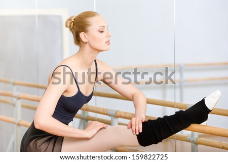 Ballet dancer stretches herself near barre and mirrors in the dancing hall