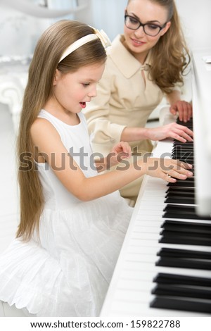 Tutor teaches little girl to play piano. Concept of music study and enjoyment