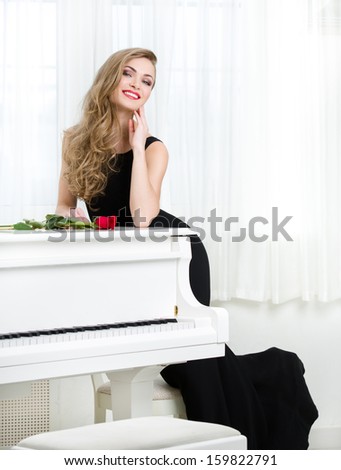 Full-length portrait of woman in black dress standing near the piano with red rose on it. Concept of music and creative hobby