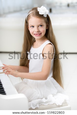 Portrait of little girl in white dress playing piano. Concept of music study and entertainment