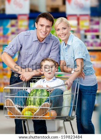 Family drives shopping trolley with food and son sitting there with watermelon. Concept of fresh and healthy food and consumerism