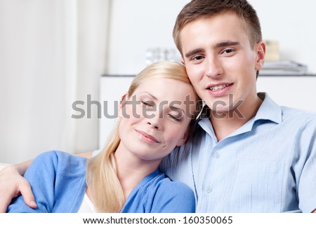 Happy couple sits on the white couch. Woman sleeps on hands of her boyfriend