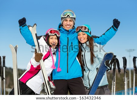 Half-length portrait of group of skier friends with hands up. Concept of cute winter sport and funny vacations with friends