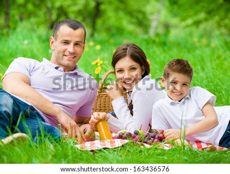 Happy Family Of Three Has Picnic In Park. Concept Of Happy Family Relations And Carefree Leisure Time
