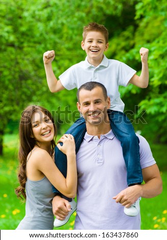 Happy Family Of Three. Dad Keeps Son On Shoulders. Concept Of Happy Family Relations And Carefree Leisure Time