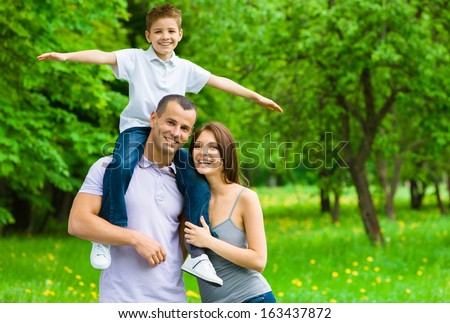 Happy Family Of Three. Father Keeps Son Airplane Gesturing On Shoulders. Concept Of Happy Family Relations And Carefree Leisure Time