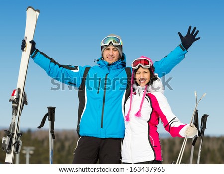 Half-length portrait of two hugging downhill skiers with skis in hands