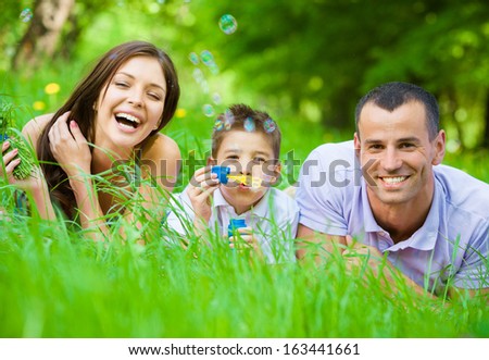 Happy family of three lying on grass while son blows bubbles. Concept of happy family relations and carefree leisure time