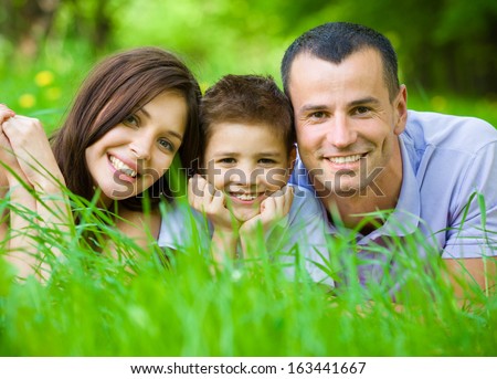 Happy Family Of Three Lying On Grass. Concept Of Happy Family Relations And Carefree Leisure Time