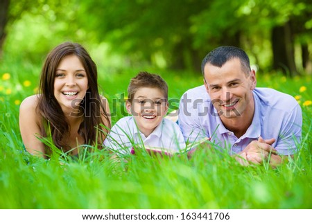 Happy family of three lying on grass while reading book. Concept of happy family relations and carefree leisure time
