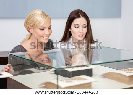 Two girls looking at showcase with jewelry at jeweler\'s shop. Concept of wealth and luxurious life