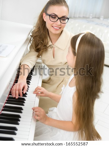 Tutor teaches little girl to play piano. Concept of music study and arts