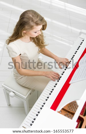 Top view of woman wearing beige dress and playing piano. Concept of music and art