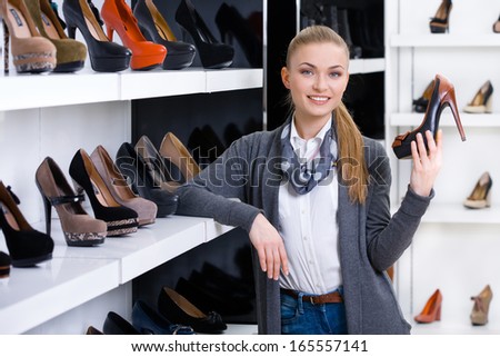 Woman with shoe in hand chooses stylish pumps looking at the shelves with numerous pumps
