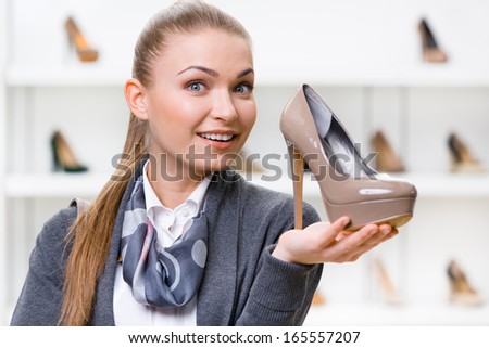 Portrait of woman keeping coffee-colored shoe in shopping center against the showcase with pumps