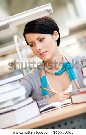 Woman surrounded with piles of books reads sitting at the table at the reading hall. Academic achievement
