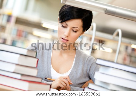 Woman surrounded with piles of books reads sitting at the table at the library. Training process