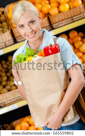 Girl hands bag with fresh vegetables against the shelves of fruits in the shopping mall