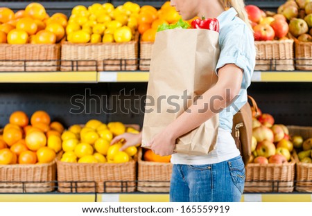 Choosing lemons girl hands bag with fresh vegetables against the shelves of fruits in the shop
