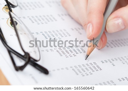 Close up of hand writing in the document with pencil. Spectacles lying on the paper