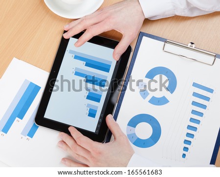 Top view of business man working on the tablet with diagrams. Close up of hands and graphs