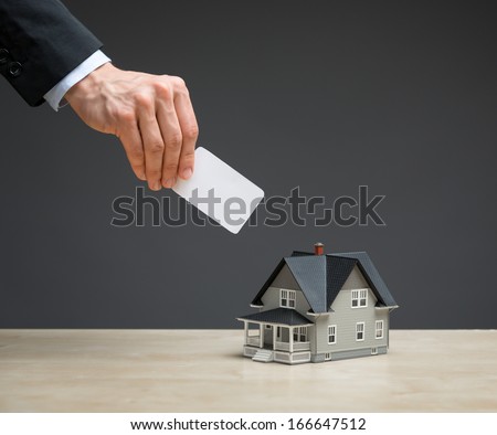 Close up of little house and hand with copyspace on grey background. Concept of real estate and investment