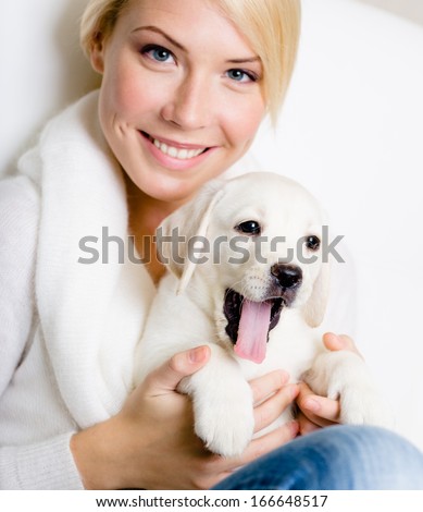 Close up of woman in white sweater with white Labrador puppy sitting on her knees and yawning