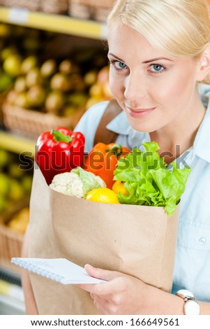 Reading list of products girl hands bag with fresh vegetables against the shelves of fruits in the store