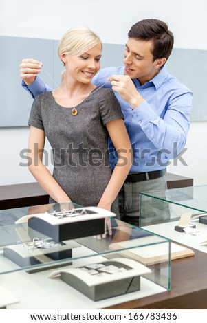 Male puts necklace on his girlfriend at jeweler\'s shop. Concept of wealth and luxurious life