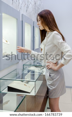 Half-length portrait of girl looking at jewelry in showcase at jeweler\'s shop. Concept of wealth and luxurious life