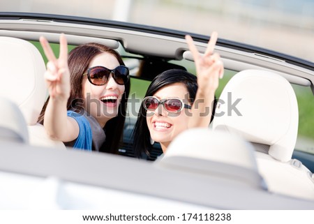 Two happy girls sitting in the car and gesturing victory sign look back and have fun while having little car trip
