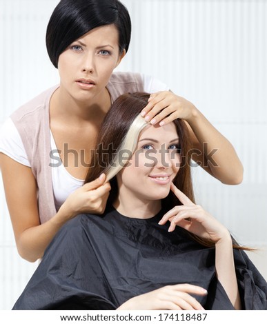Hair Stylist Tries Lock Of Dyed Blond Hair On The Client Sitting On The Chair In The Hairdressing Salon