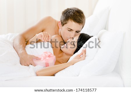 Man lying in bed gives present wrapped with pink paper to lady