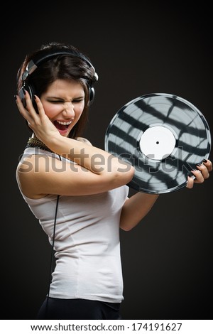 Half-length portrait of pretty teenager with earphones and record in hands on grey background. Concept of rock music and arts