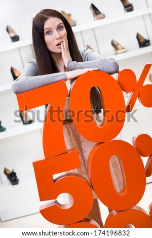 Woman showing the percentage of sales on footwear in the shopping center against the window case with pumps