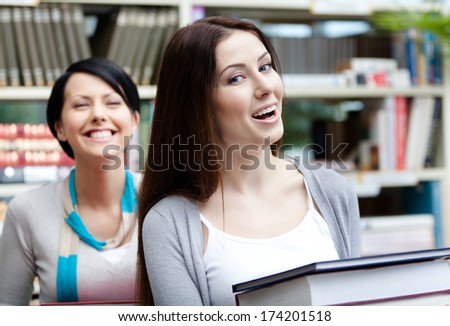 Two laughing girlfriends carry piles of books at the library