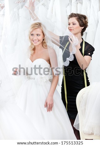 Shop assistant puts wedding veil on the head of the bride, white background
