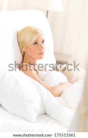 Pensive woman lying in bed under the warm blanket