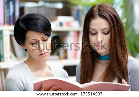 Two sad female students read books at the library