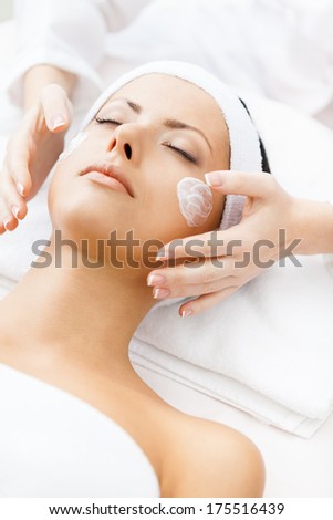 Hands of therapist apply cream to face of woman. Concept of care and youth