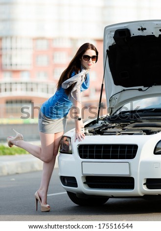 Woman repairing the broken car on the street. Girl stands near opened hood of the car after an accident
