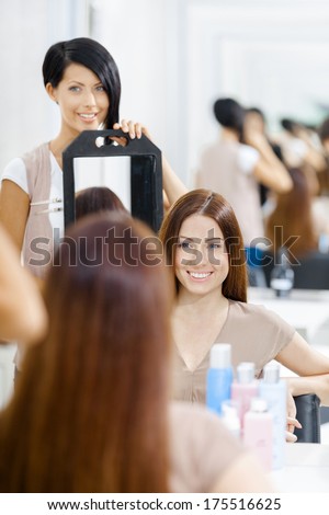 Hair stylist showing the ready hairstyle of the female client in mirror. Concept of fashion and beauty