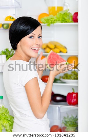 Girl takes watermelon from the opened fridge full of vegetables and fruit. Concept of healthy and dieting food
