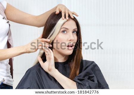 Hairdresser tries lock of dyed blond hair on the client sitting on the chair in the hairdress salon