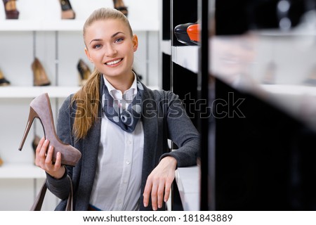 Woman with shoe in hand chooses shoes looking at the shelves with numerous pumps