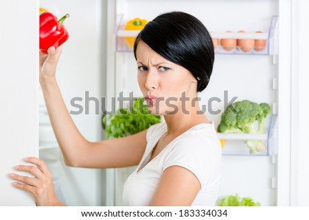 Woman takes bell pepper from the opened fridge full of vegetables and fruit. Concept of healthy and dieting food