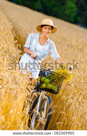 Girl rides bicycle with apples and flowers in rye field. Concept of rural lifestyle and sport