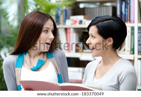 Two amazed female students read books at the library